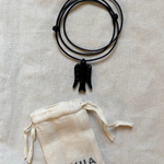 Black leather bracelet with tassel on a beige fabric background with 'ASHIA' pouch.